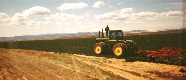 アメリカの農業研修プログラムで配属されたコロラド州 の高地で運転するトラクター(ジョンディア)の上に立つ岡元さん
